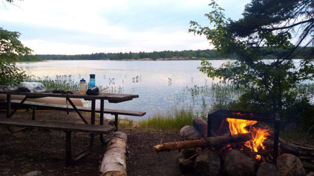 View of the lake from my campground on Pakeshkag Lake. Picnic table and fire pit with fire in the foreground.