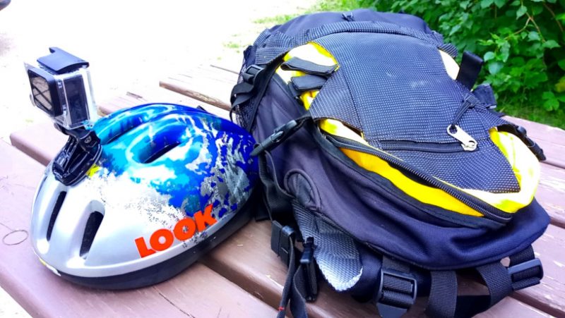 Picture of a backpack and bicycle helmet with goPro attached sitting on a picnic table