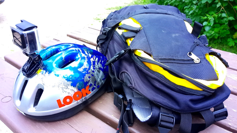 Picture of a backpack and bicycle helmet with goPro attached sitting on a picnic table